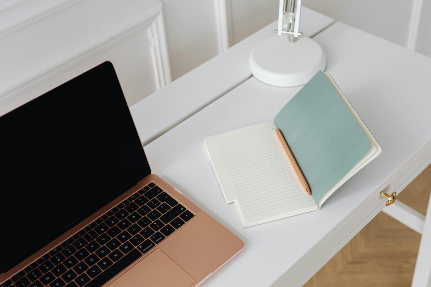 En öppen anteckningsbok på ett skrivbord bredvid en öppen laptop